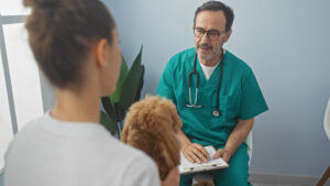 female-pet-owner-holding-poodle-dog-in-her-lap-while-talking-with-male-vet-at-clinic