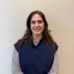 Female with long brown wearing a blue vest with a gray long sleeved tshirt underneath