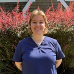 female standing in front of a bush wearing blue scrubs